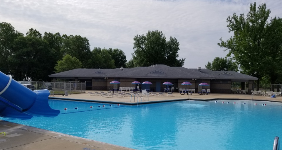 Outdoor community pool with a blue waterslide and pool house at Roxana Community Park