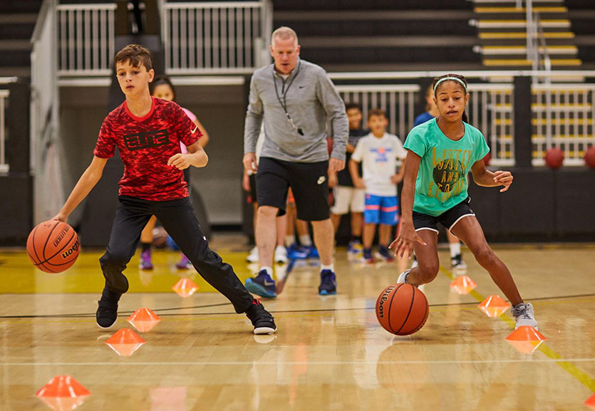 Young players dribbling around cones while a coach watches