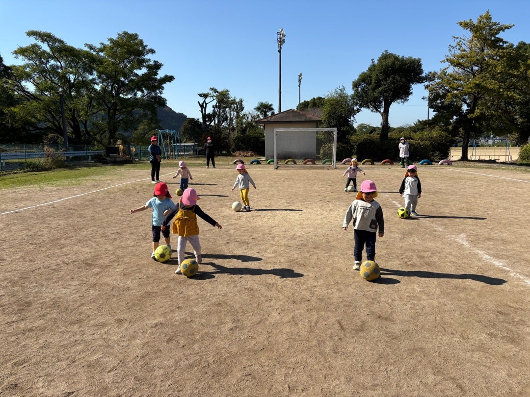 Very young children, each with their own soccer ball, spread out on a sunny soccer field