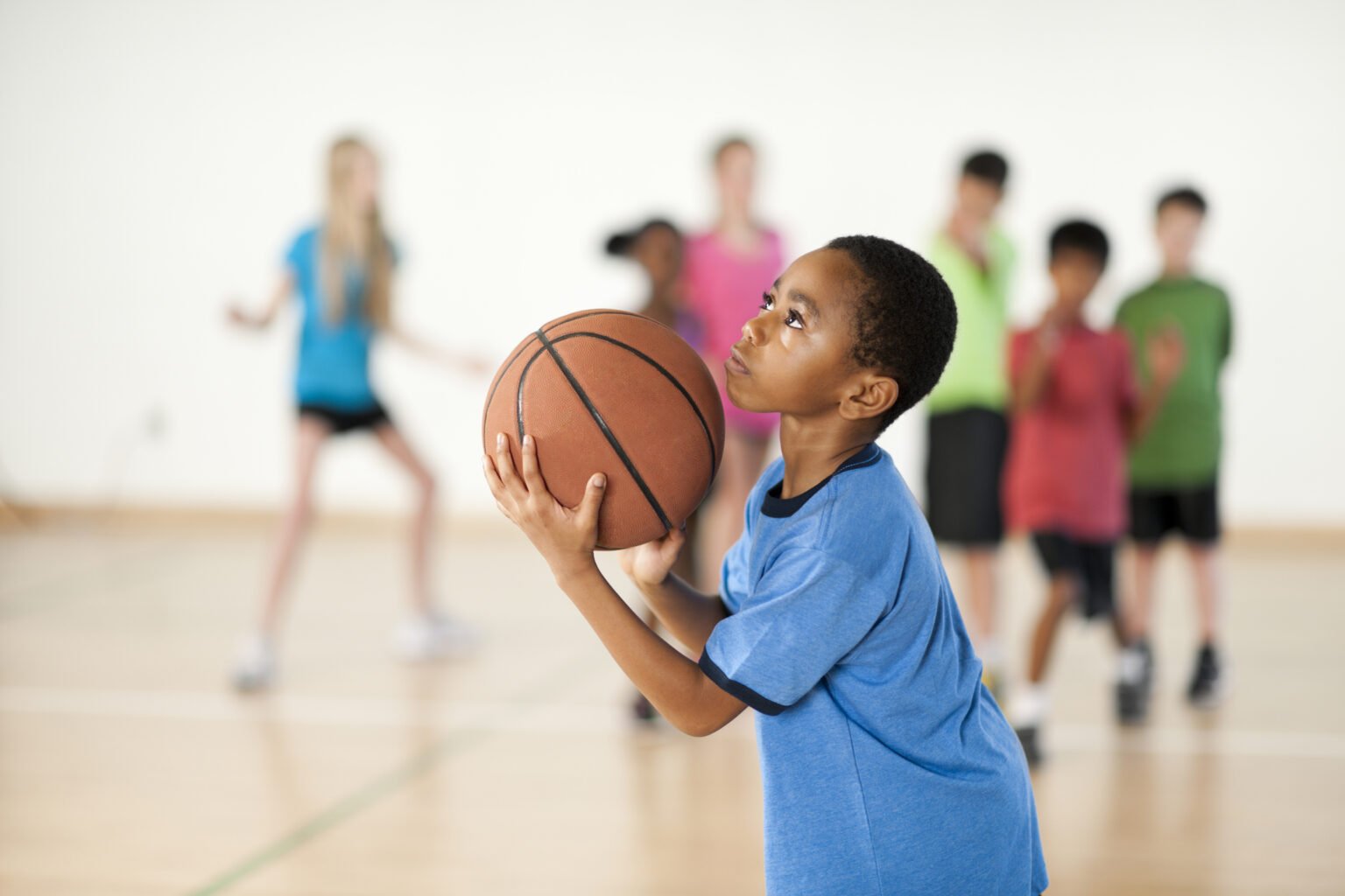 A young player holding a basketball, getting set to shoot in a gym