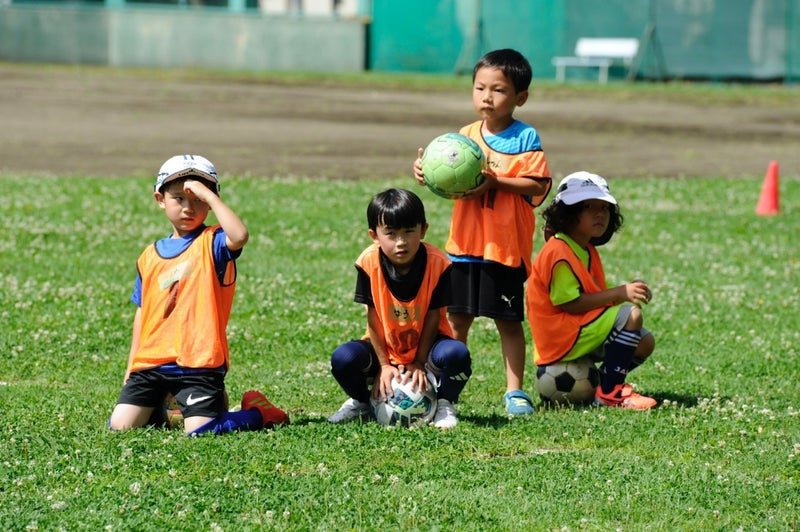 Young players in orange bibs resting on the grass with their soccer balls